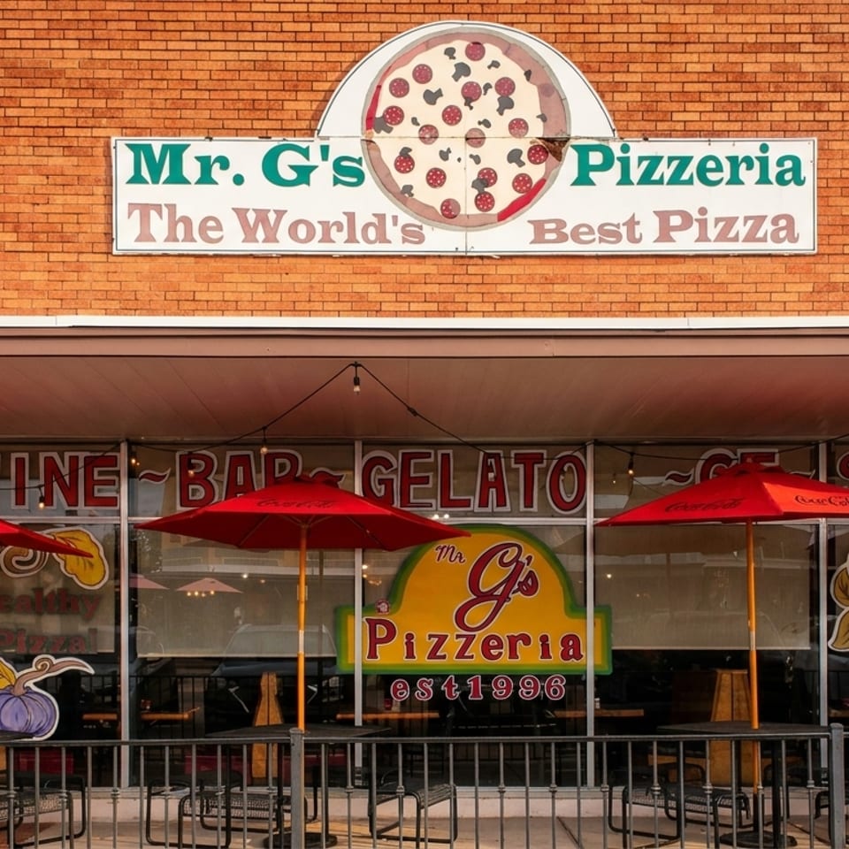 Mr. G's Pizzeria storefront with red umbrellas, outdoor seating, and a brick facade.