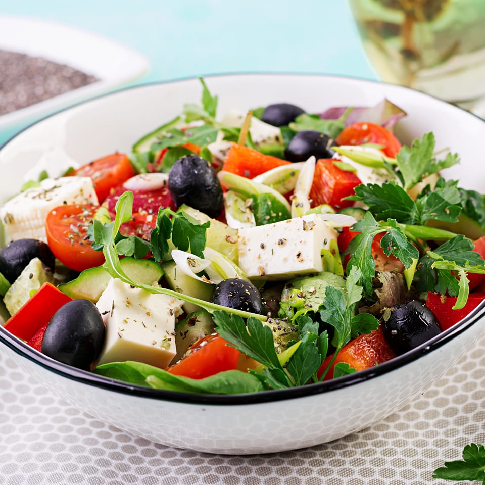 Fresh Greek salad with feta cheese, tomatoes, olives, cucumber, and herbs in a white bowl.