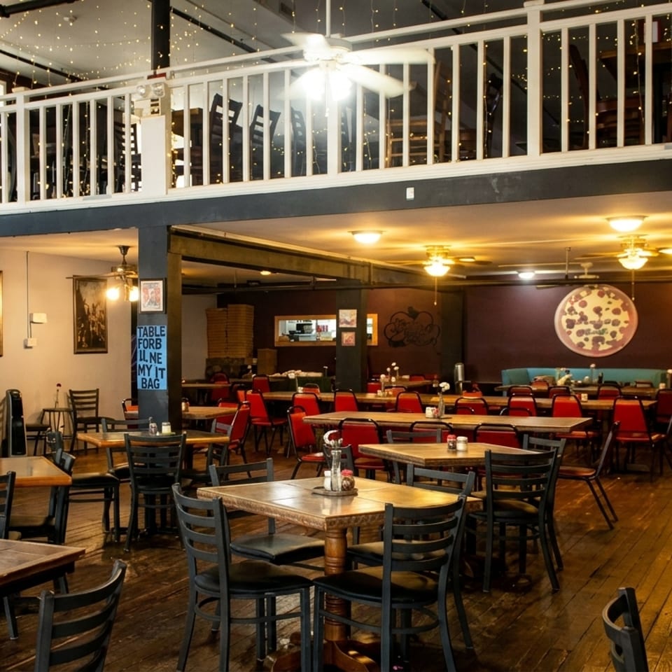 Spacious restaurant interior with wooden tables, red chairs, a balcony, and string lights.