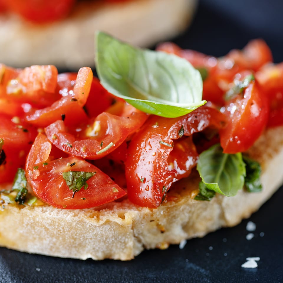 Close-up of fresh bruschetta with diced tomatoes, herbs, and a basil leaf on toasted bread.